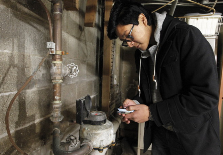 Student checks a water meter in a basement and logs the reading on his phone